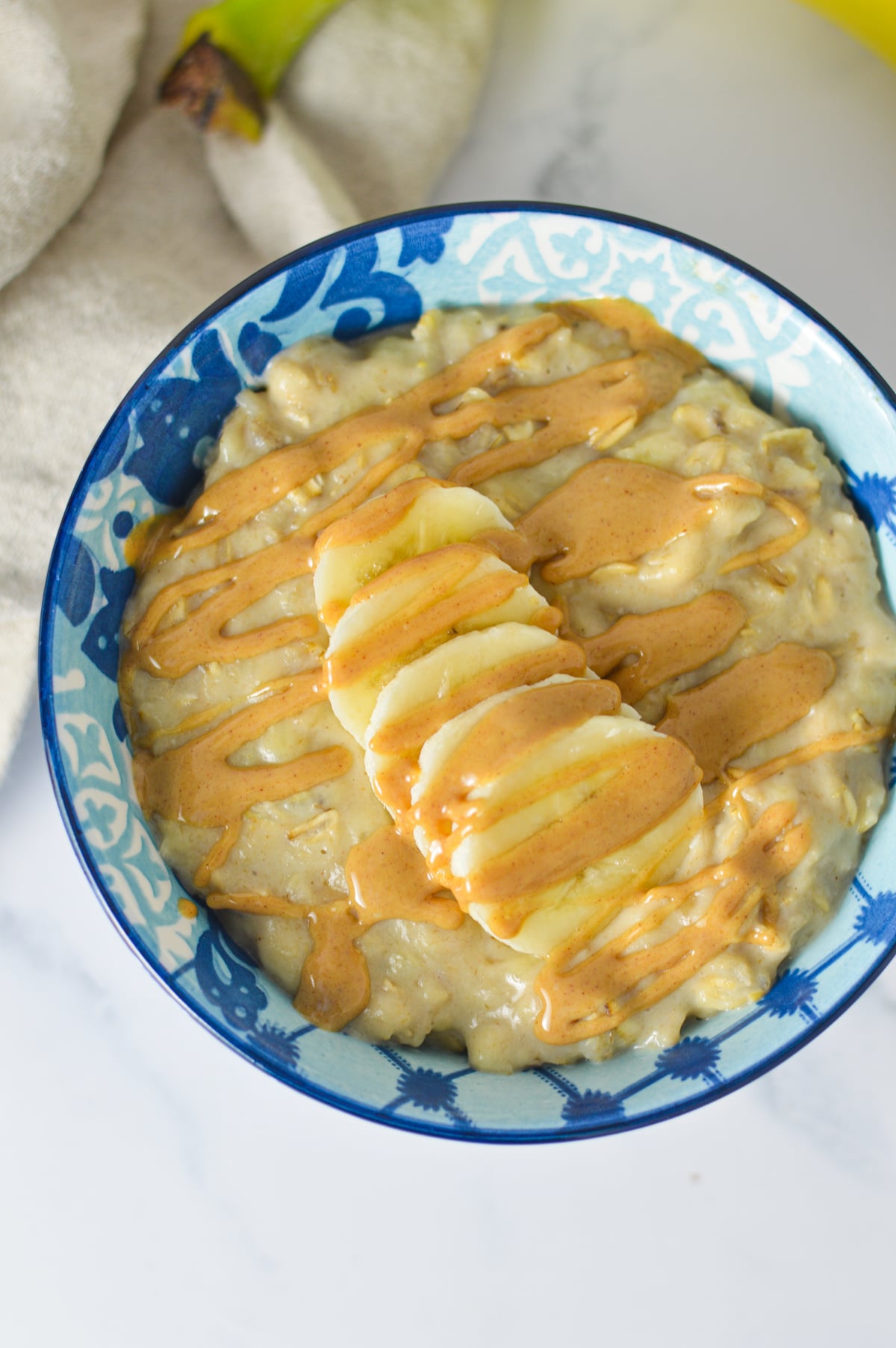 A bowl of warm peanut butter banana oatmeal topped with sliced bananas and a drizzle of peanut butter.