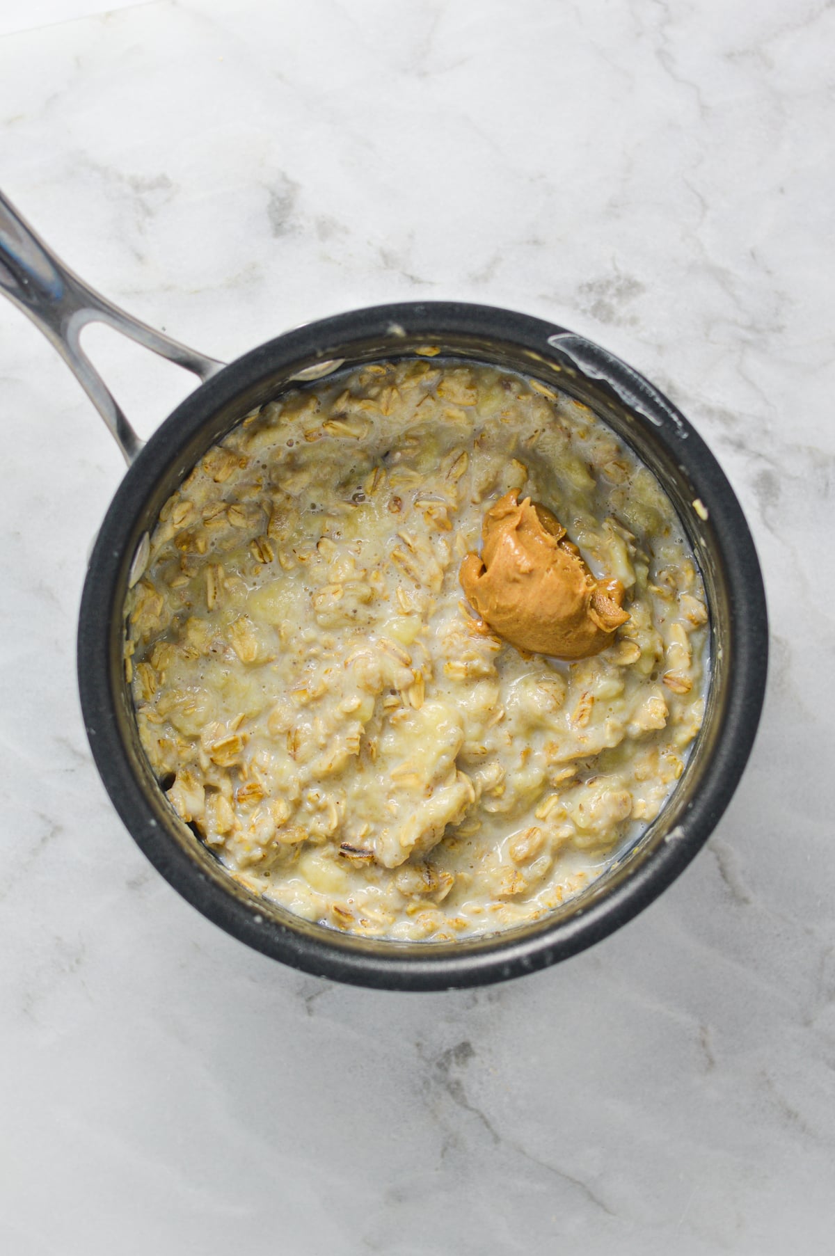 Freshly cooked oats in a small saucepan, with a dollop of peanut butter on top.