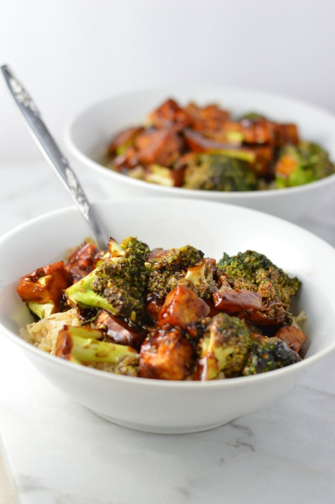 Two white medium sized bowls filled with Tofu Sesame Broccoli Stir Fry on a bowl of brown rice.