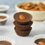 A stack of Almond Mini Nutella Cups with the paper liners taken off, and a bowl of whole almonds in the background.