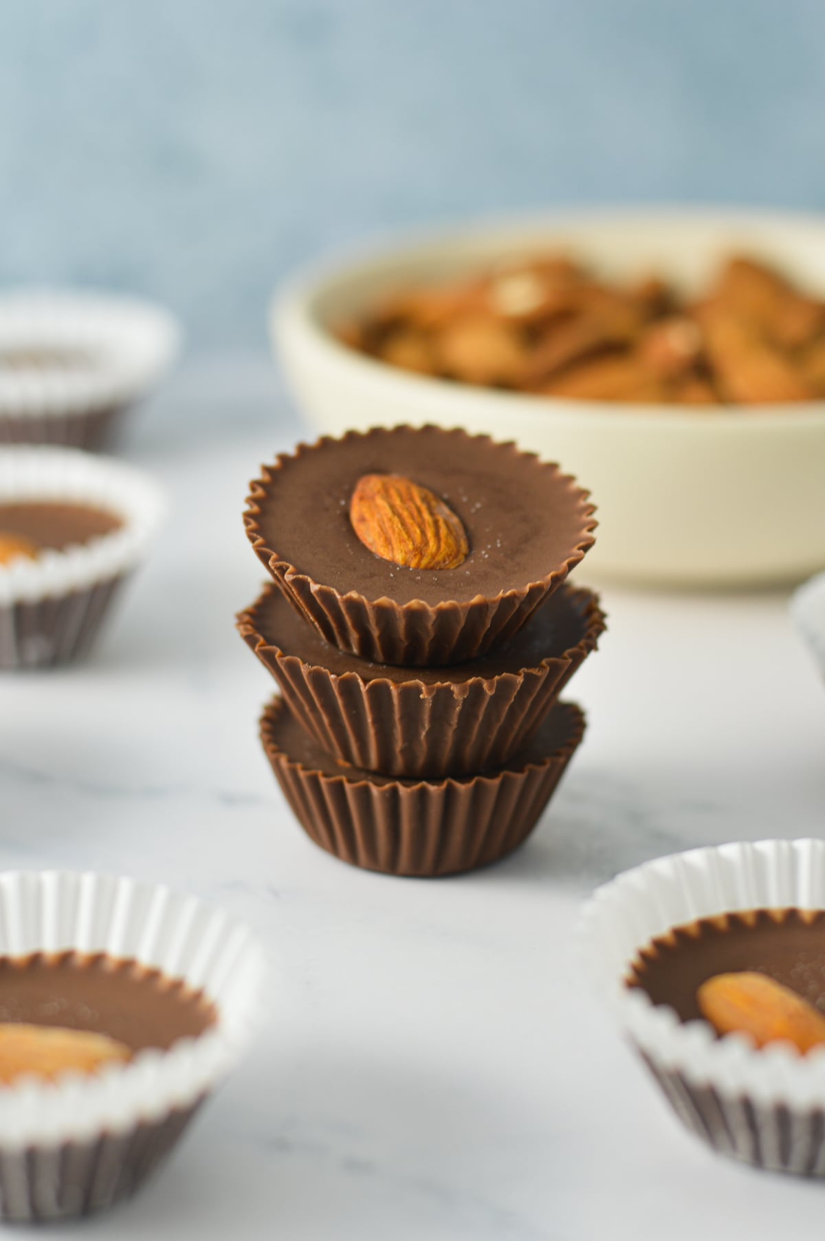 A stack of Almond Mini Nutella Cups with the paper liners taken off, and a bowl of whole almonds in the background.