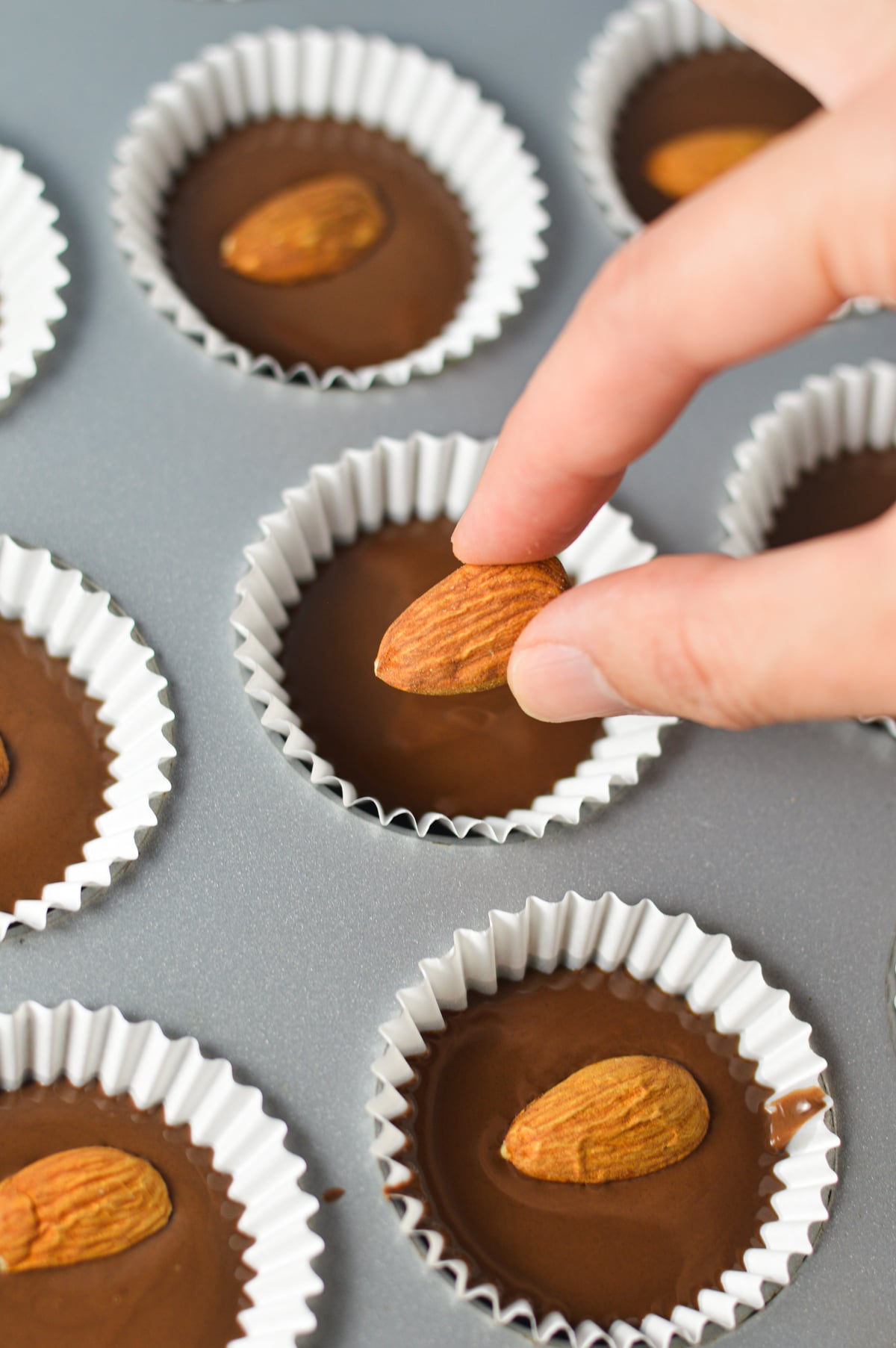 A hand placing some whole almonds on top of Nutella cups in a paper lined mini muffin pan.