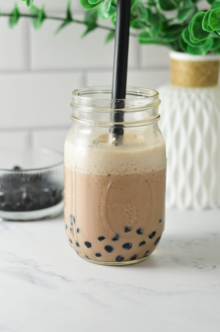 A mason jar filled with chocolate bubble tea and tapioca pearls, served with a black boba straw.