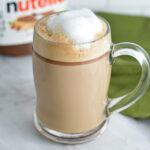 Nutella Latte with foamy milk on top, and a jar of Nutella in the background.