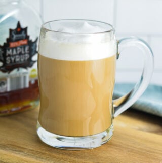 Maple Latte in a glass cup, with a maple syrup container in the background.