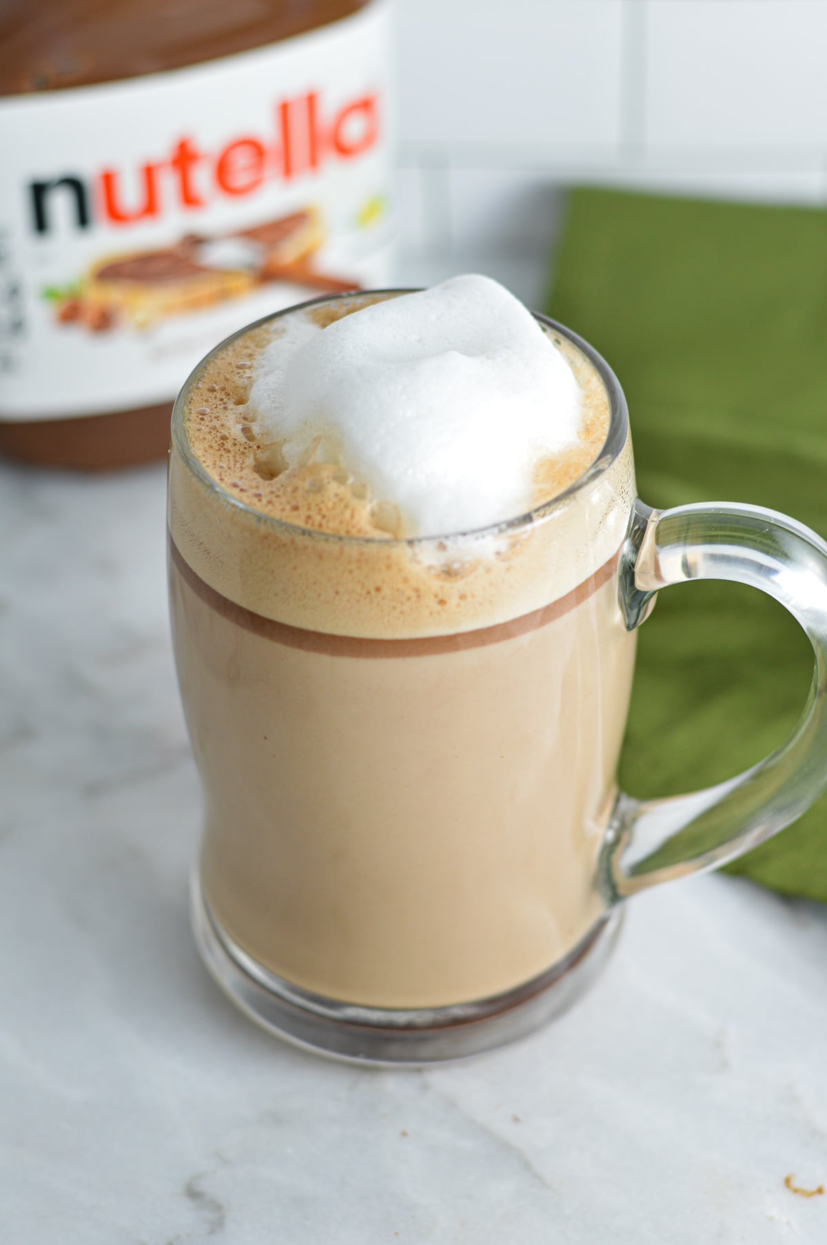 Nutella Latte with foamy milk on top, and a jar of Nutella in the background.