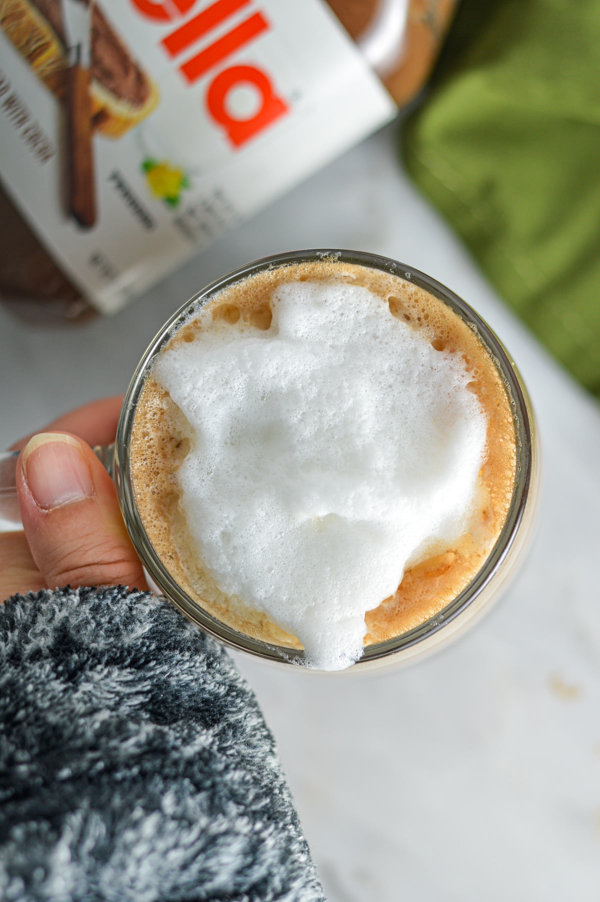 A hand holding a mug with Nutella Latte and frothed milk in it.