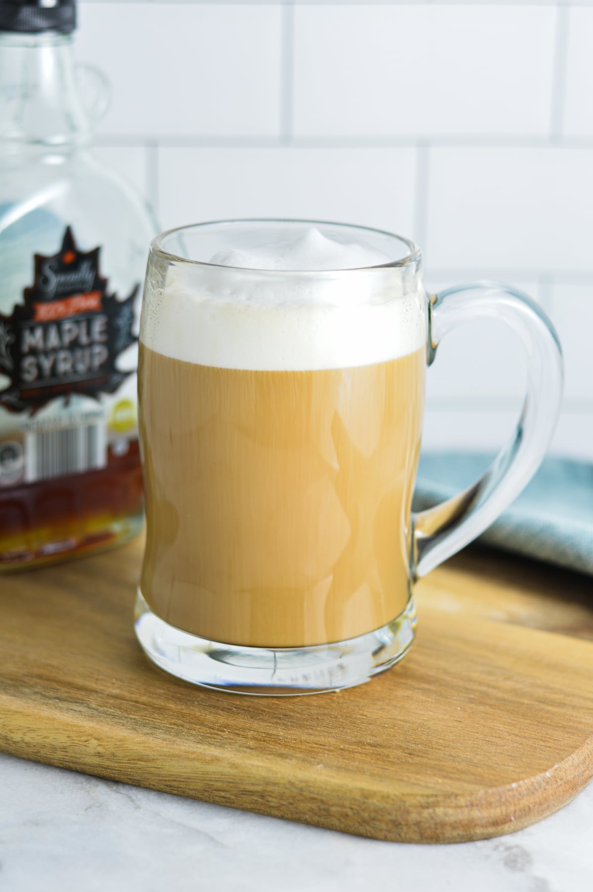 Maple Latte in a glass mug with a jar of maple syrup in the background.