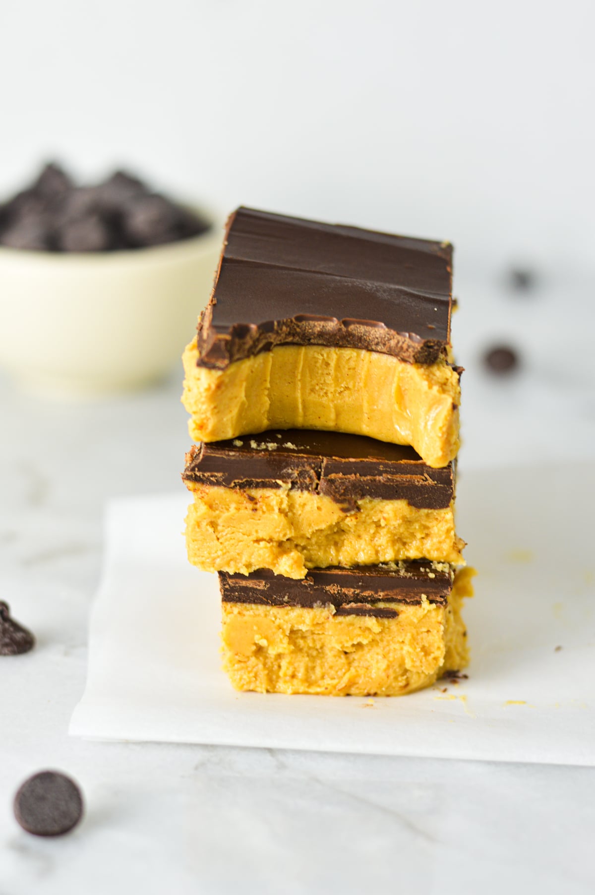A stack of three homemade no-bake Buckeye Bars cut into neat squares, showcasing a thick, creamy peanut butter base and a smooth, rich chocolate top layer.