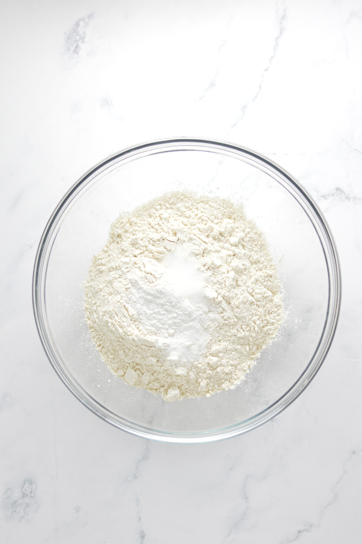 The flour, baking powder, baking soda and salt for the banana bread donuts in a medium sized glass bowl.