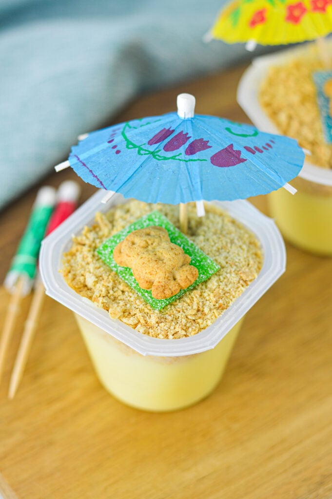 Sand Pudding Cups with cocktail umbrellas sticking out of the crushed graham cracker layer.