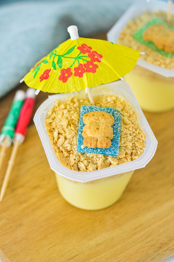 Sand Pudding Cups with a teddy graham on top of a sour strip candy resembling a beach scene.