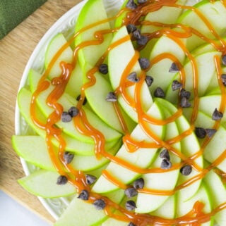 Apple Nachos for One on a small plate with a drizzle of caramel sauce and mini chocolate chips on top.
