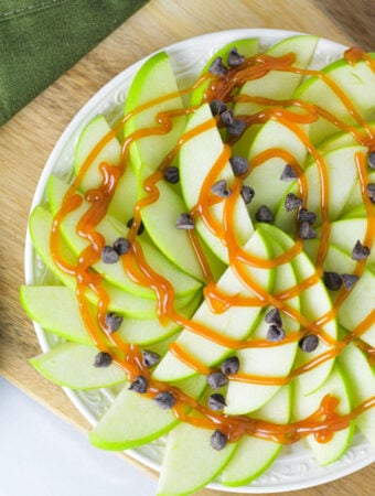 Apple Nachos for One on a small plate with a drizzle of caramel sauce and mini chocolate chips on top.
