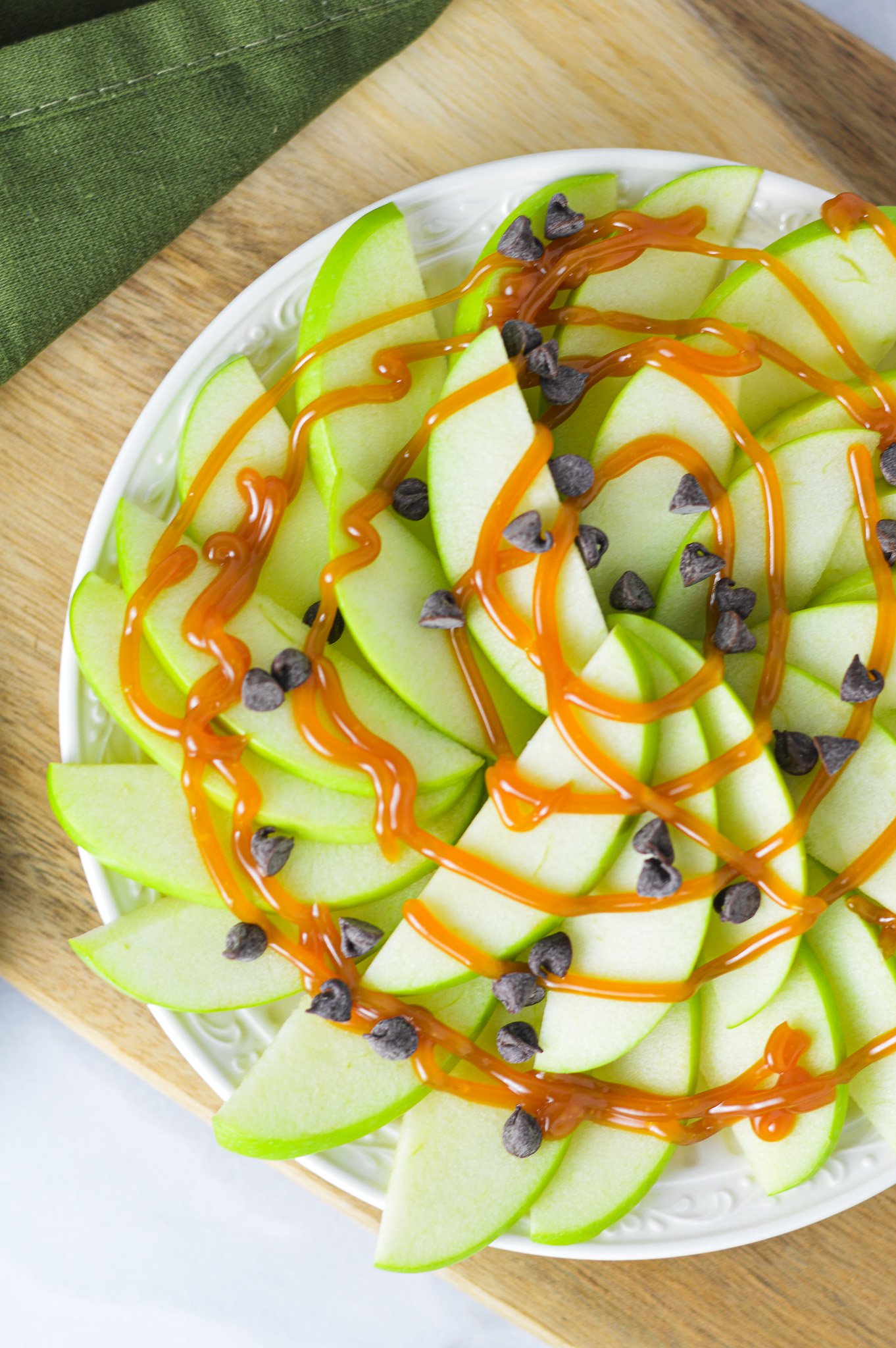 Apple Nachos for One on a small plate with a drizzle of caramel sauce and mini chocolate chips on top.