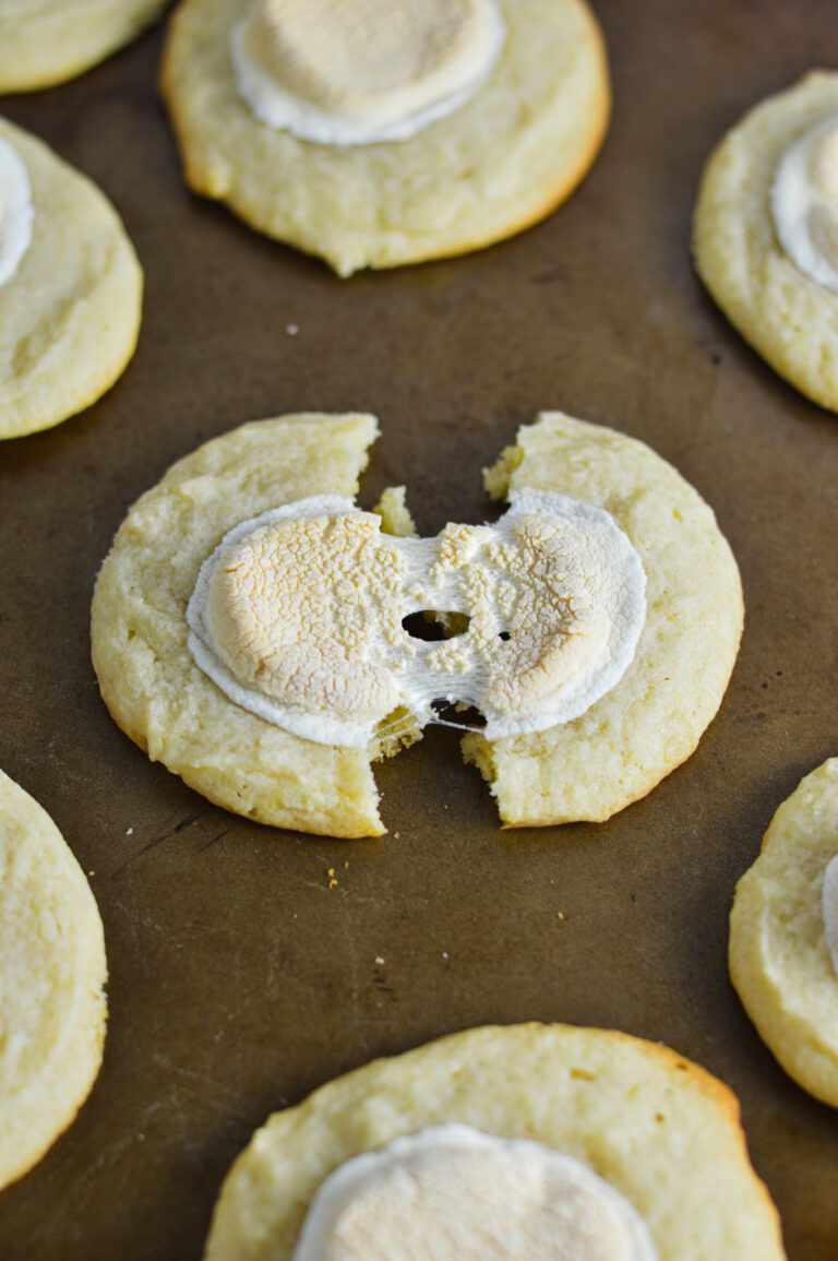 White Hot Chocolate Cookies on a cookie sheet, with a cookie cut in half showing the melted marshmallow topping.