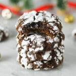A stack of Peppermint Chocolate Crinkle Cookies with a bite taken out of the top one, revealing a fudgy interior.