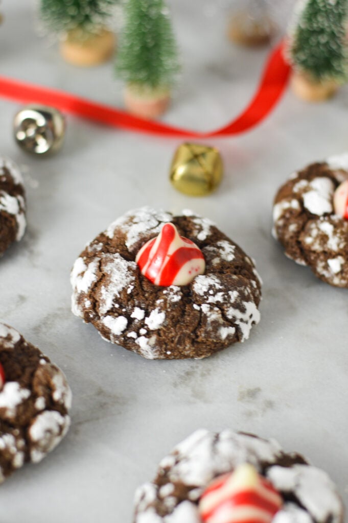 Peppermint Kiss Chocolate Crinkle Cookies on a granite surface with bells and red ribbon in the background, adding to a festive feel.
