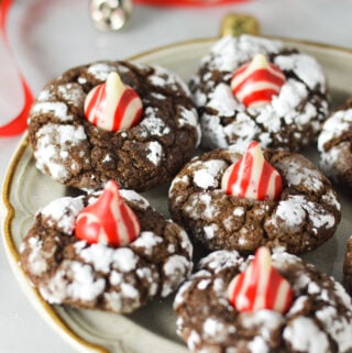 Peppermint Kiss Chocolate Crinkle Cookies on a small plate, with Christmas bells and wrapping ribbon in the background, giving it a Christmassy feel.