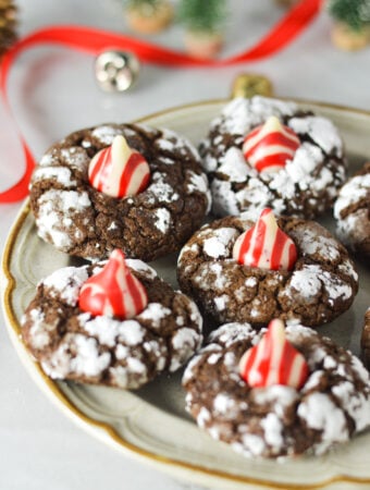 Peppermint Kiss Chocolate Crinkle Cookies on a small plate, with Christmas bells and wrapping ribbon in the background, giving it a Christmassy feel.