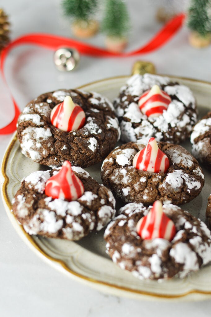 Peppermint Kiss Chocolate Crinkle Cookies on a small plate, with Christmas bells and wrapping ribbon in the background, giving it a Christmassy feel.