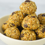A small shallow bowl filled with Almond Peanut Butter Chocolate Energy Bites, showing its hearty texture filled with chia seeds, chocolate chips and rolled oats.