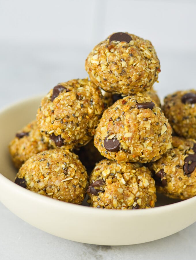 A small shallow bowl filled with Almond Peanut Butter Chocolate Energy Bites, showing its hearty texture filled with chia seeds, chocolate chips and rolled oats.
