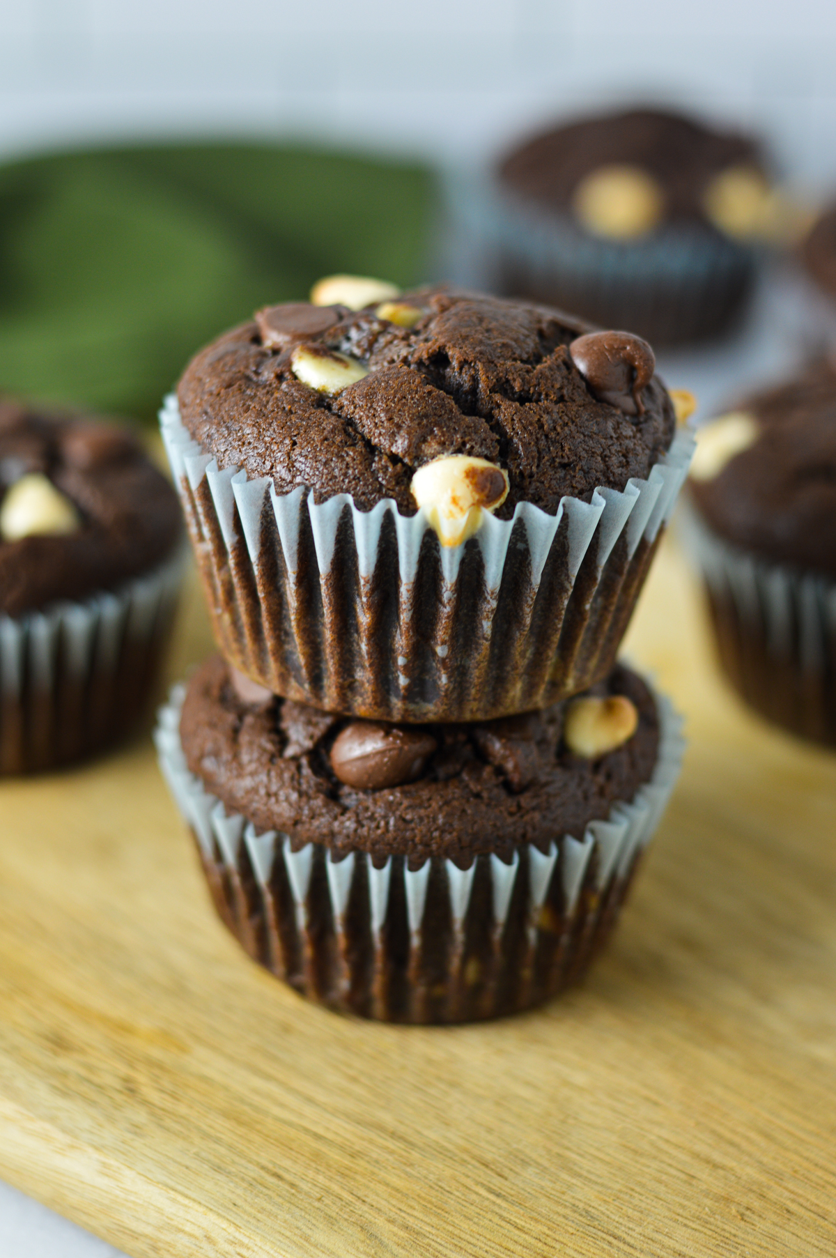 A stack of fluffy Triple Chocolate Banana Muffins, with both white and semi sweet chocolate chips covering the top of each rich muffin.