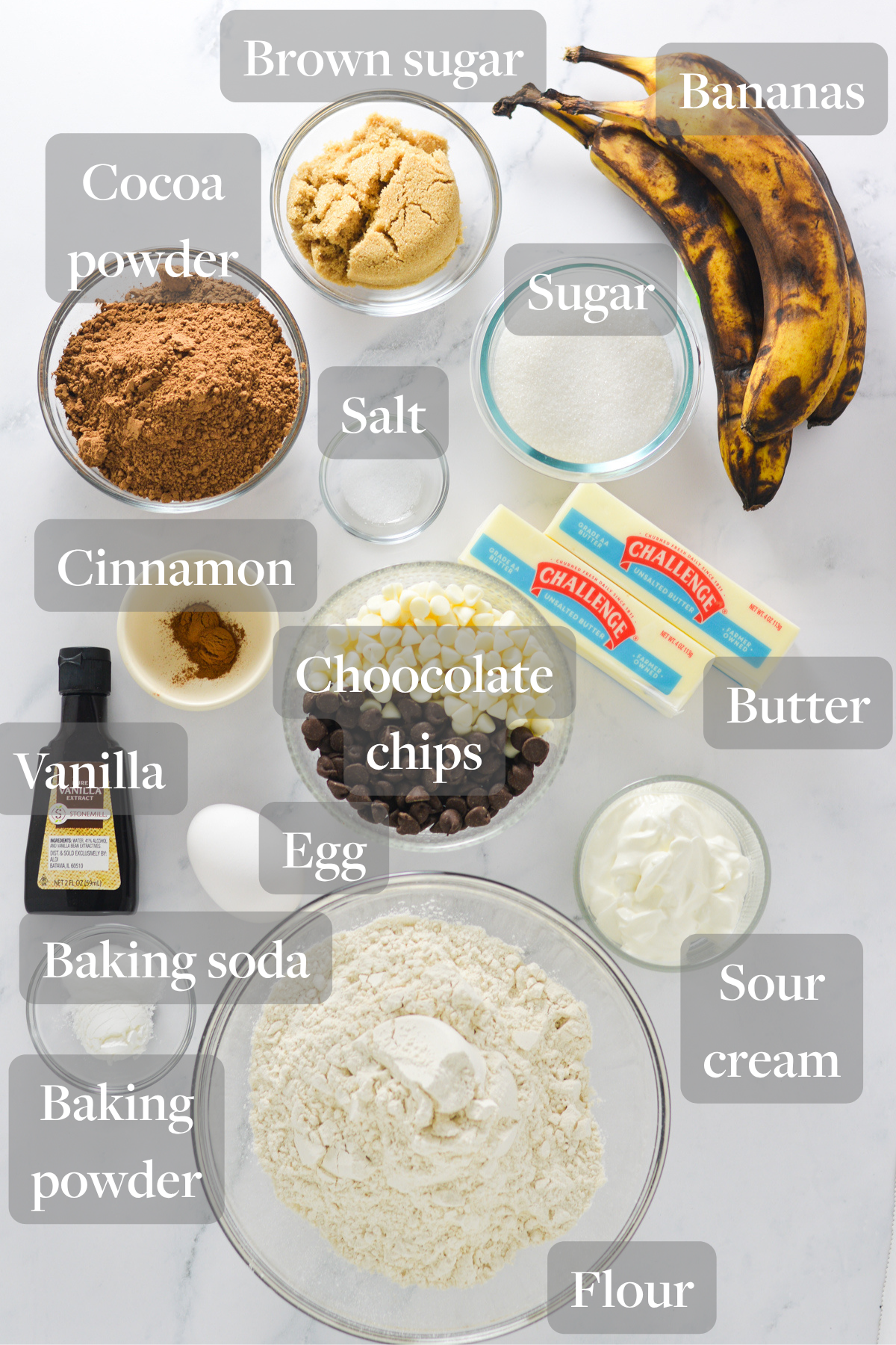 All the ingredients required to make Triple Chocolate Banana Muffins laid out on a marble surface.