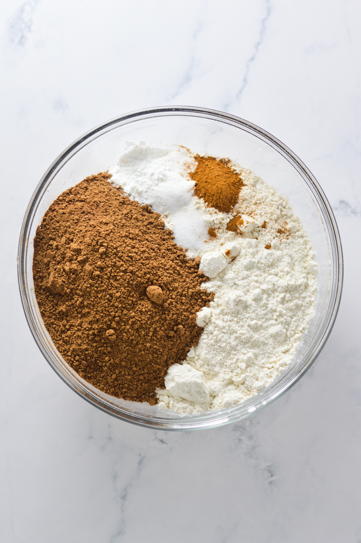 A large glass bowl filled with all-purpose flour, cocoa powder, baking soda, baking powder, salt and ground cinnamon.