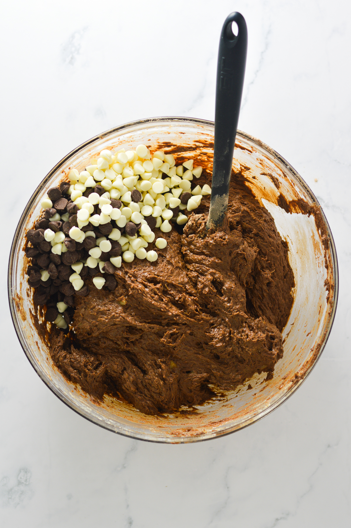 The wet and dry ingredients mixed together in a large bowl, with semi-sweet and white chocolate chips on top of the batter.