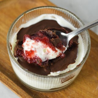 A Chocolate Covered Strawberry Yogurt Bowl, with a spoon taking out a bite, clearly showing the layers of creamy yogurt, strawberry jam and magic shell.
