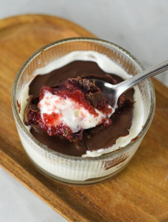 A Chocolate Covered Strawberry Yogurt Bowl, with a spoon taking out a bite, clearly showing the layers of creamy yogurt, strawberry jam and magic shell.