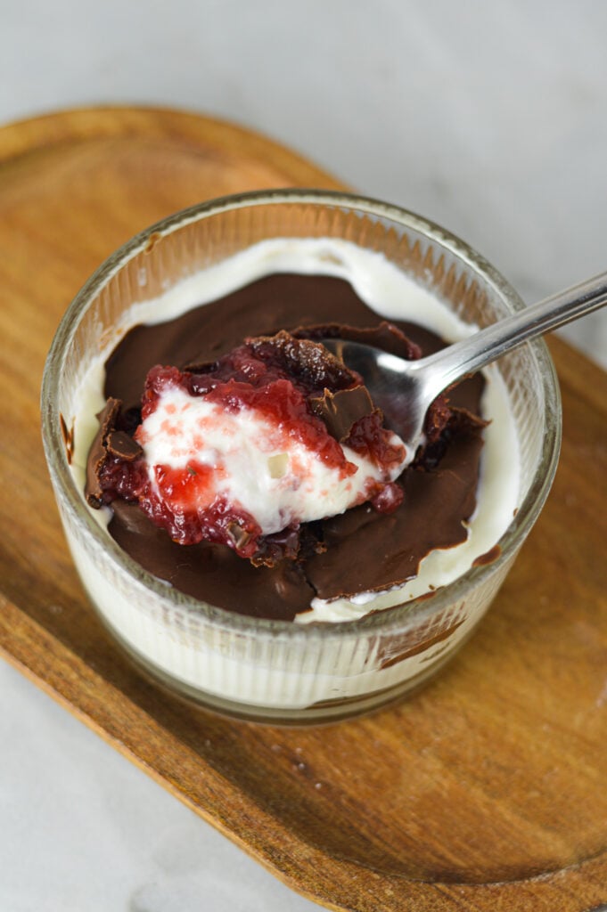 A Chocolate Covered Strawberry Yogurt Bowl, with a spoon taking out a bite, clearly showing the layers of creamy yogurt, strawberry jam and magic shell.