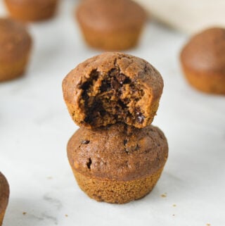 A stack of Double Chocolate Mini Muffins with a bite taken out of the top muffin, showing the rich and fluffy texture.