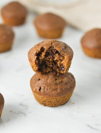 A stack of Double Chocolate Mini Muffins with a bite taken out of the top muffin, showing the rich and fluffy texture.