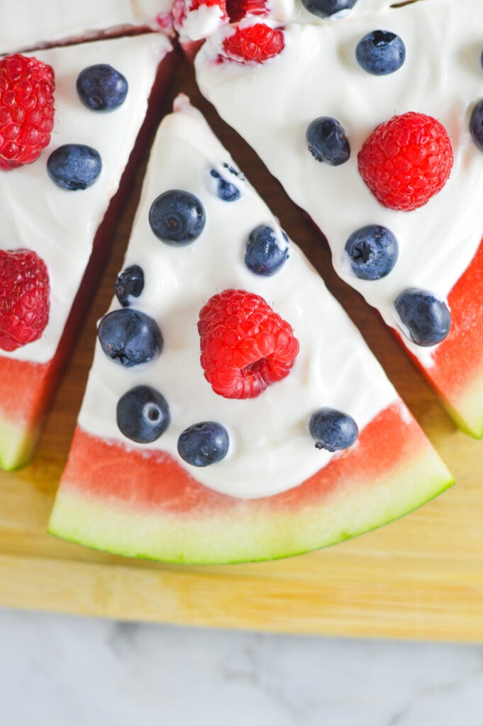 Healthy Watermelon Pizza topped with fresh berries and Greek yogurt on a wooden cutting board.