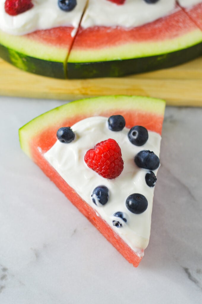 A slice of Healthy Watermelon Pizza topped with fresh blueberries, raspberries and Greek yogurt.