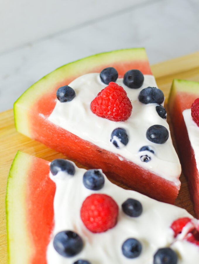 Sliced Healthy Watermelon Pizza, topped with fresh raspberries, blueberries and Greek yogurt.