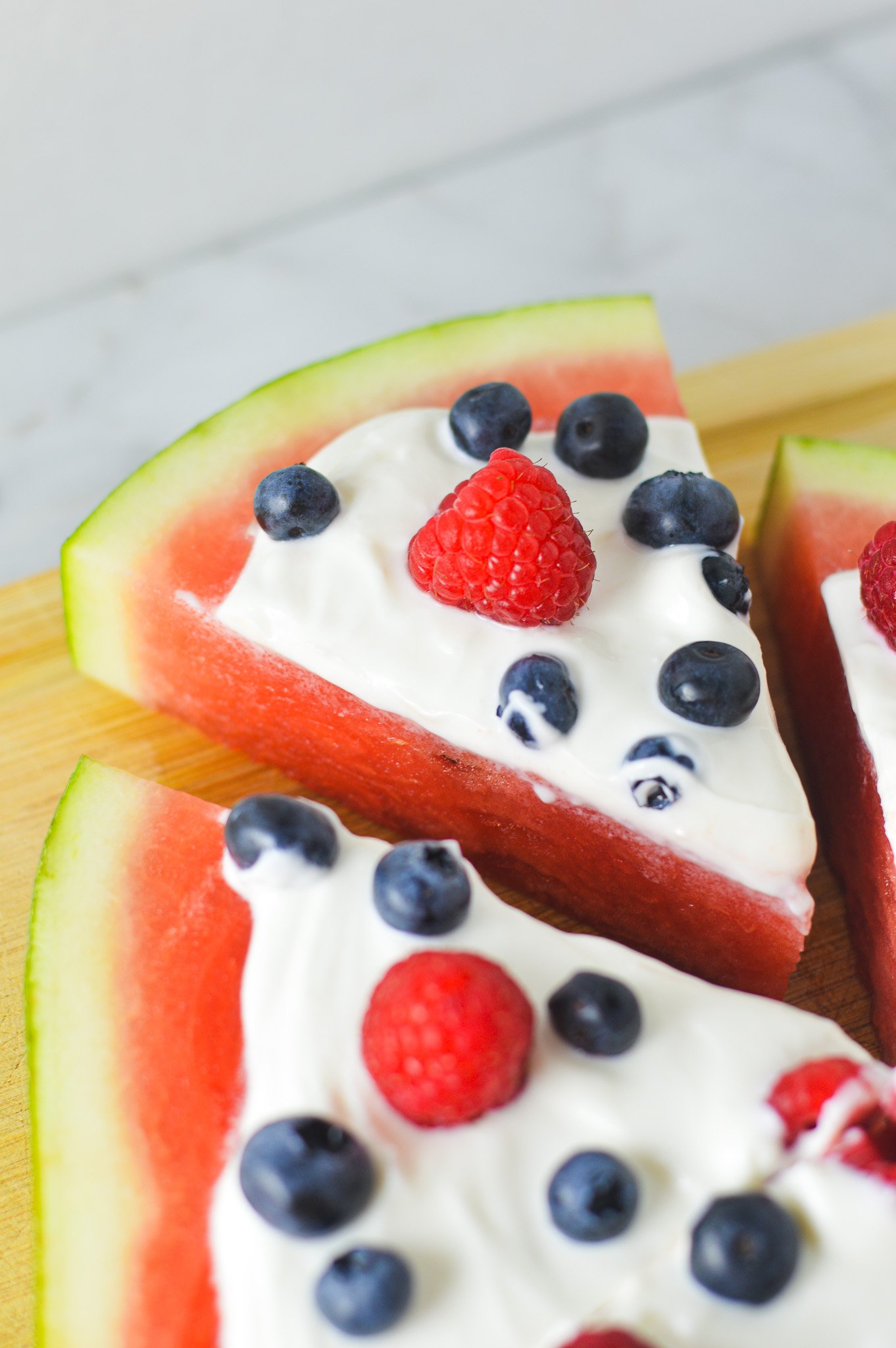 Sliced Healthy Watermelon Pizza, topped with fresh raspberries, blueberries and Greek yogurt.