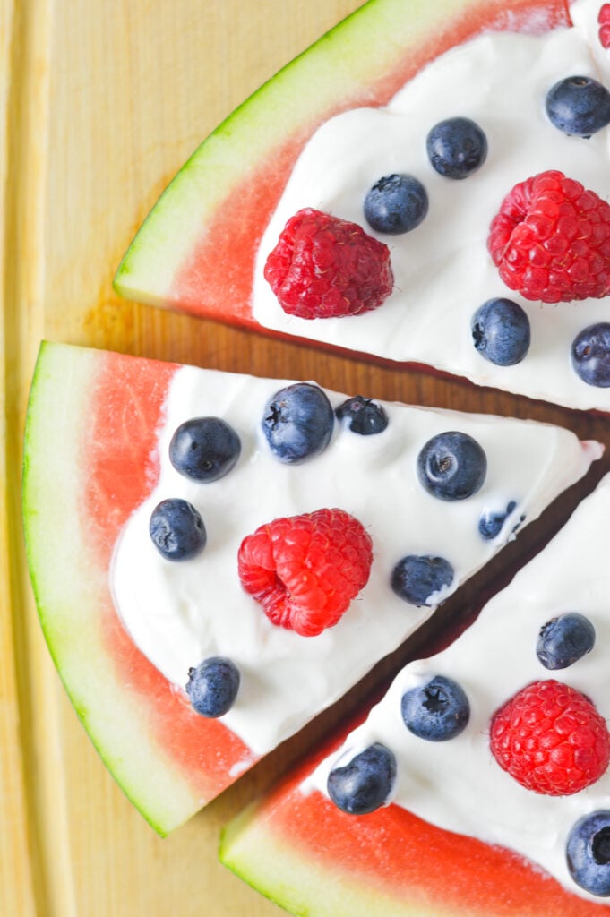 A fresh and healthy Healthy Watermelon Pizza, topped with Greek yogurt and fresh berries, on a wooden cutting board.