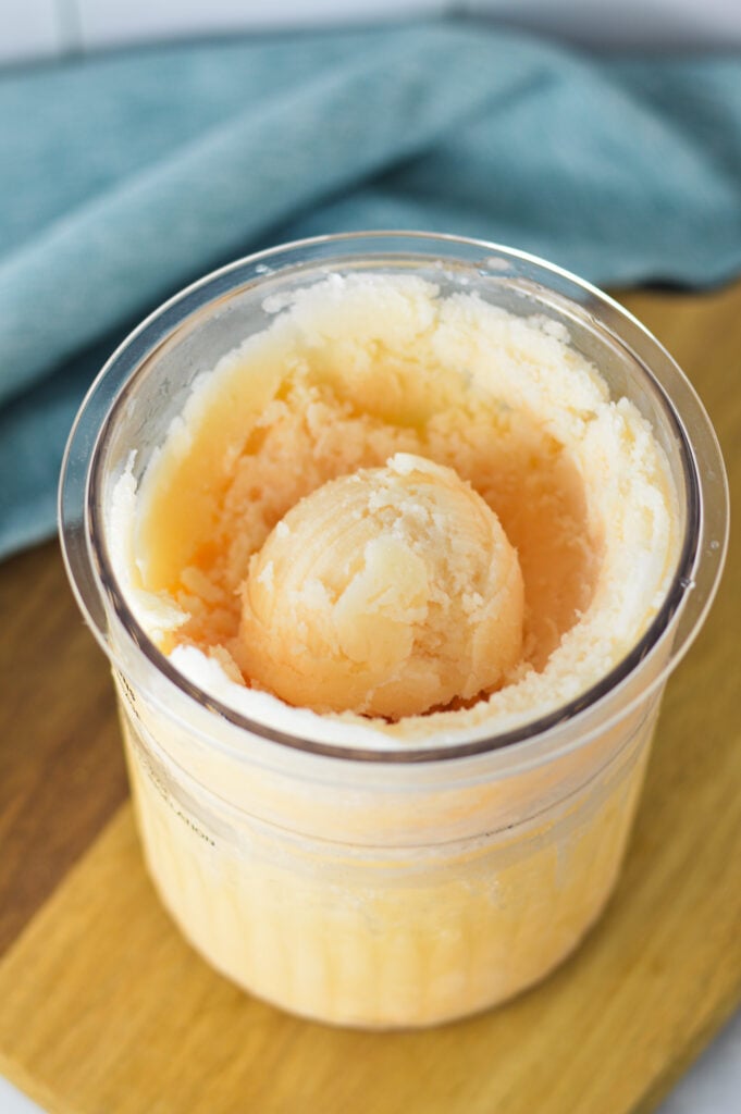 A Ninja Creami pint full of Ninja Creami Grapefruit Italian Ice, with an icy scoop in the center.