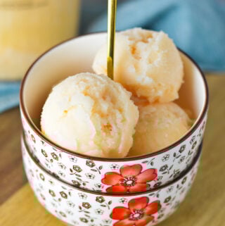 A bowl of homemade Ninja Creami Grapefruit Italian Ice, with a Ninja Creami pint full of the Italian ice in the background.