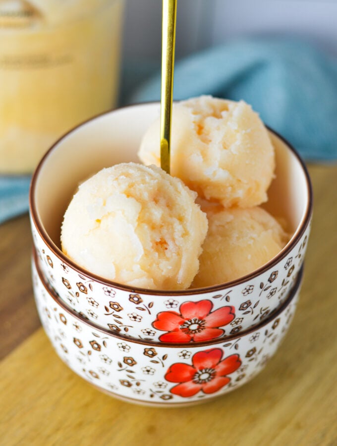 A bowl of homemade Ninja Creami Grapefruit Italian Ice, with a Ninja Creami pint full of the Italian ice in the background.