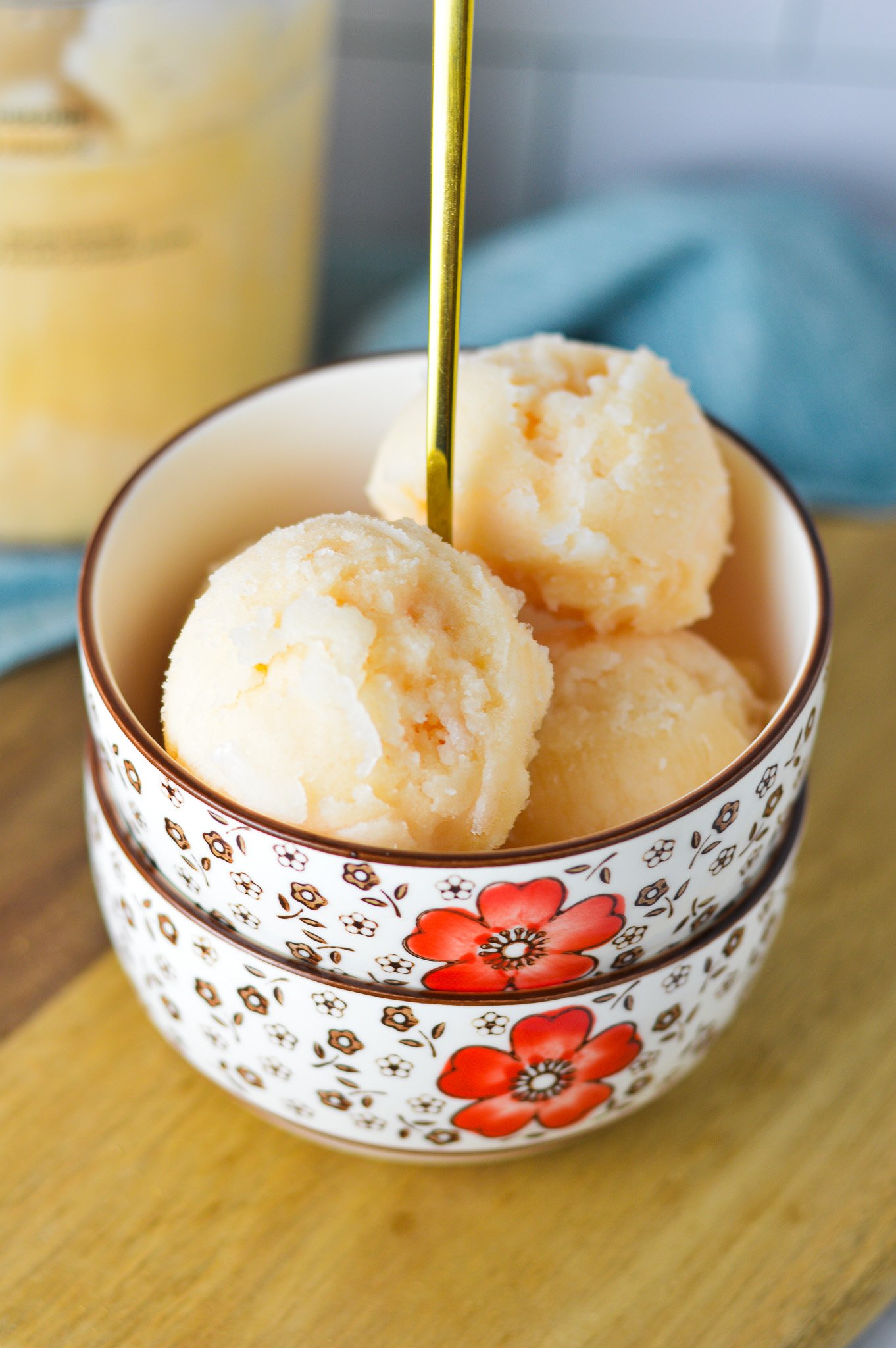 A bowl of homemade Ninja Creami Grapefruit Italian Ice, with a Ninja Creami pint full of the Italian ice in the background.