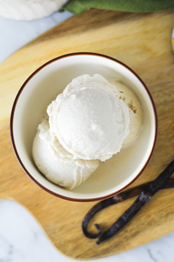 Ninja Creami Vanilla Bean Ice Cream in a small bowl, with some vanilla beans in the background.