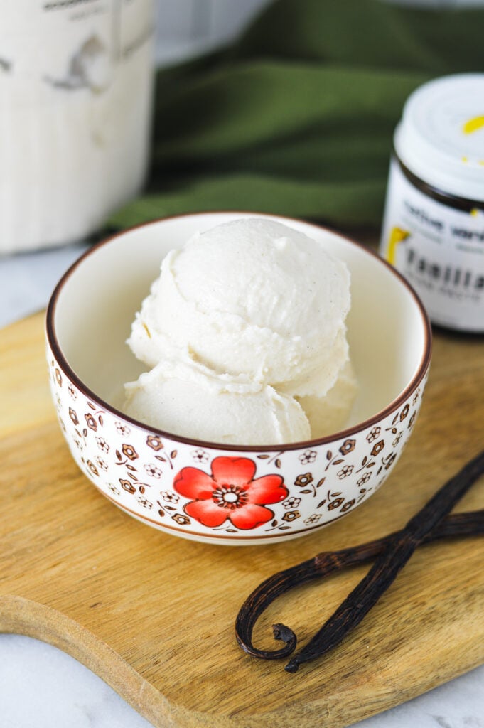 Ninja Creami Vanilla Bean Ice Cream with a jar of vanilla paste and vanilla beans in the background.