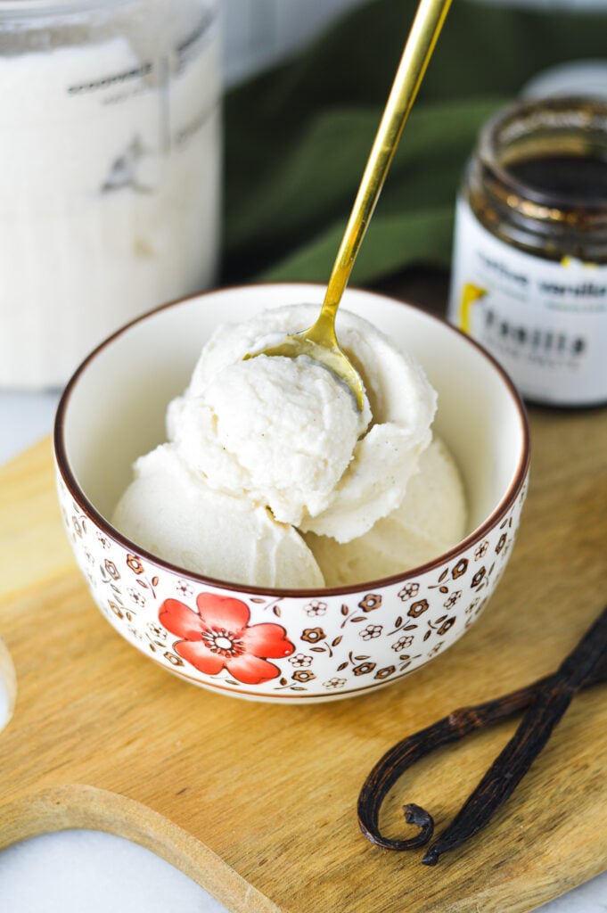 A small spoon sticking out of a bowl full of Ninja Creami Vanilla Bean Ice Cream, showing the rich texture of the creamy vanilla ice cream.