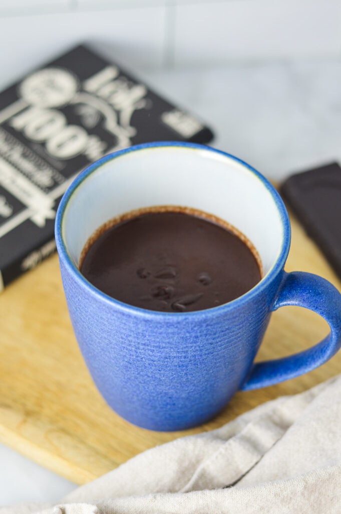 Thick Rich Hot Chocolate in a blue coffee mug, with a 100% chocolate bar in the background.