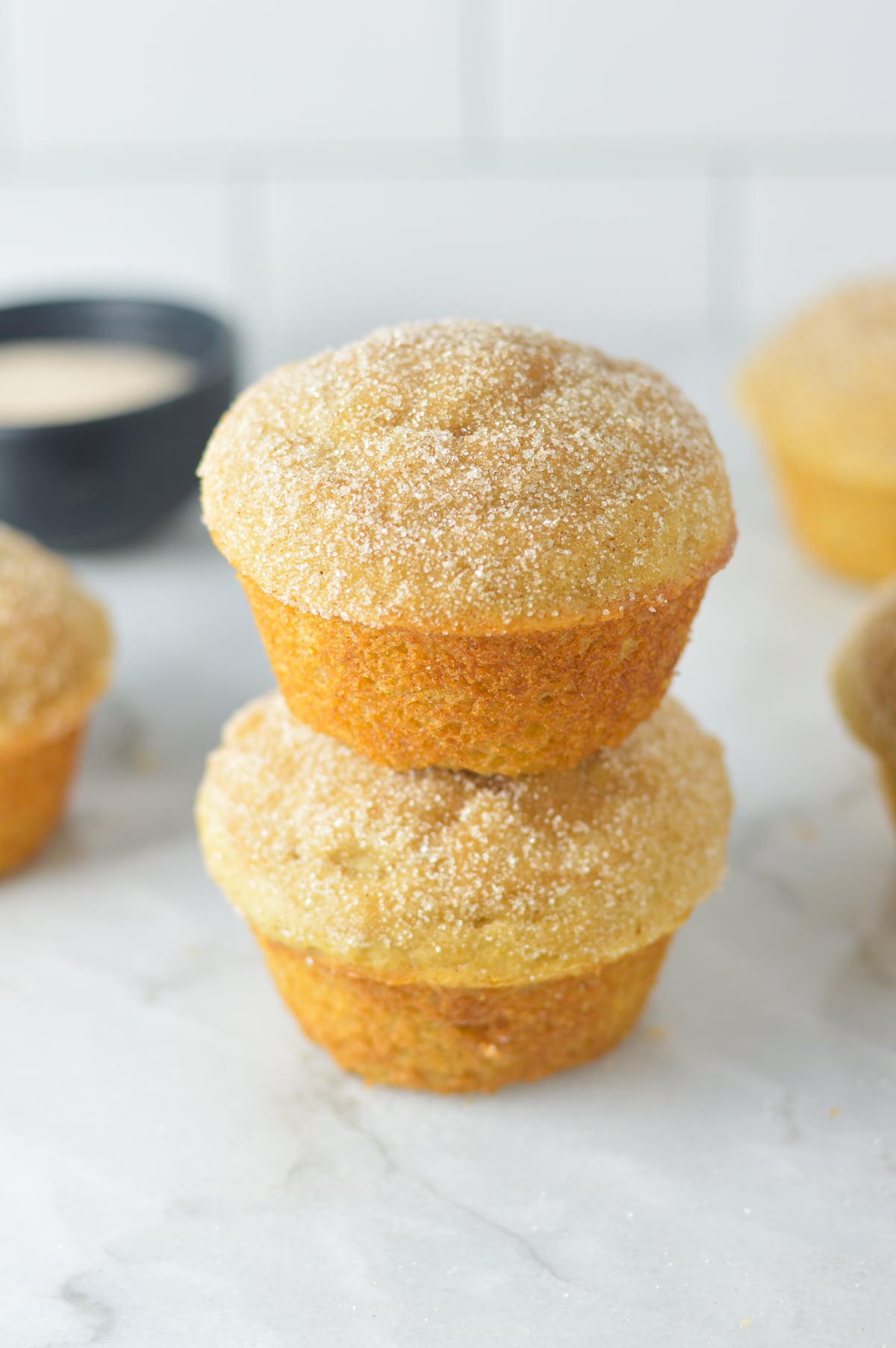A close-up stack of two golden-brown donut muffins heavily coated in cinnamon sugar.